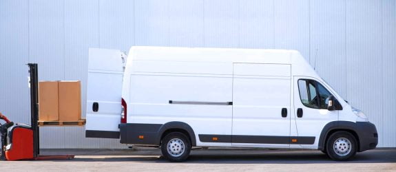 White delivery van being loaded with boxes by a forklift outside a warehouse